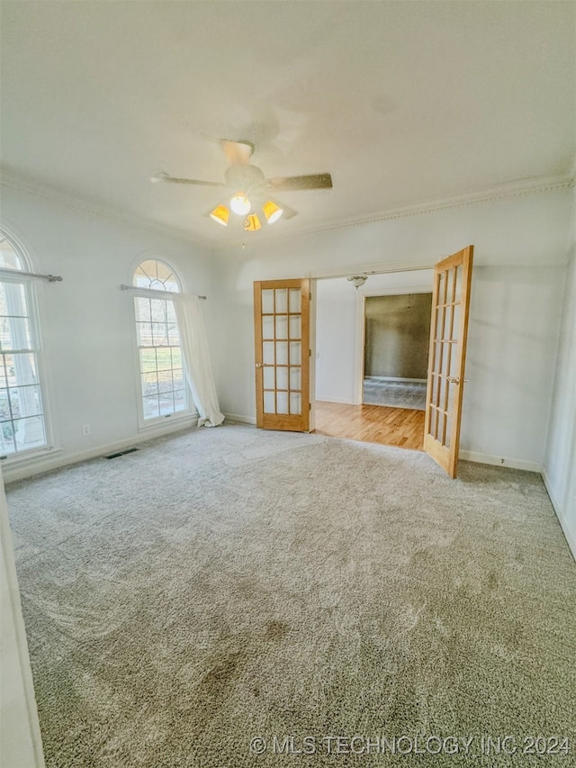 empty room featuring ceiling fan, french doors, crown molding, and light carpet