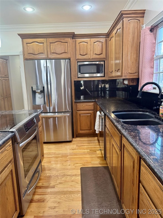 kitchen featuring sink, stainless steel appliances, light hardwood / wood-style flooring, dark stone countertops, and ornamental molding