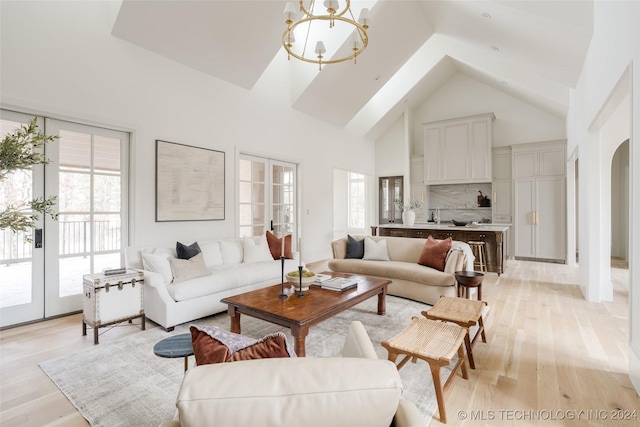 living room featuring light wood-type flooring, french doors, a towering ceiling, and a notable chandelier