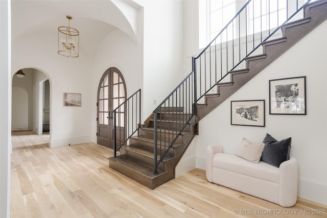 stairs featuring a towering ceiling, hardwood / wood-style flooring, and an inviting chandelier