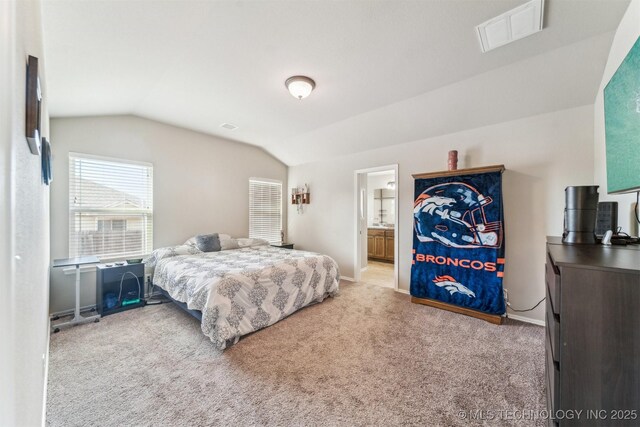 bedroom with ensuite bathroom, light carpet, and vaulted ceiling