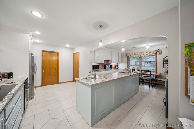 kitchen with white cabinetry, light stone countertops, stainless steel appliances, an island with sink, and pendant lighting