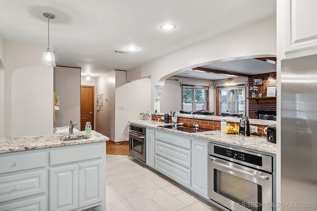 kitchen with white cabinets, sink, a fireplace, decorative light fixtures, and stainless steel appliances