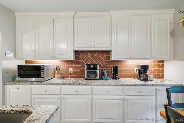 kitchen featuring light stone counters, white cabinetry, and backsplash