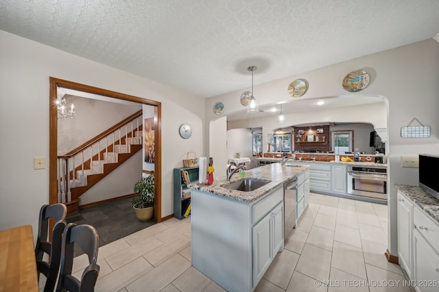 kitchen featuring light stone countertops, stainless steel appliances, sink, pendant lighting, and an island with sink