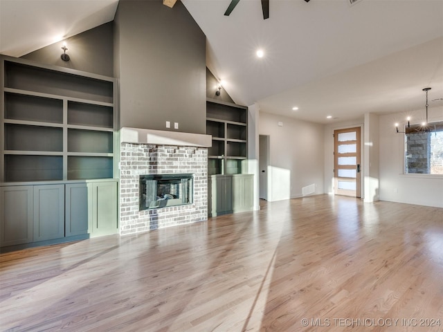 unfurnished living room featuring built in features, visible vents, light wood-style flooring, a glass covered fireplace, and ceiling fan with notable chandelier