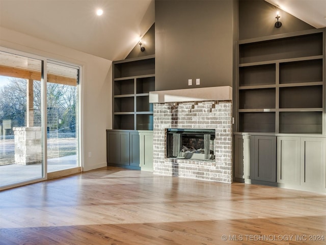 unfurnished living room featuring built in shelves, lofted ceiling, light wood-type flooring, and a brick fireplace