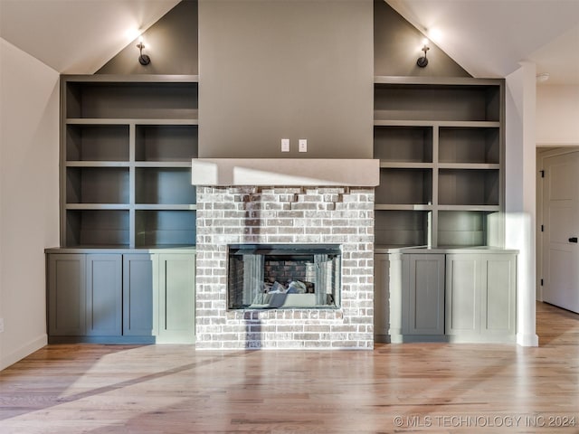 unfurnished living room with vaulted ceiling, built in features, a fireplace, and light wood-style floors