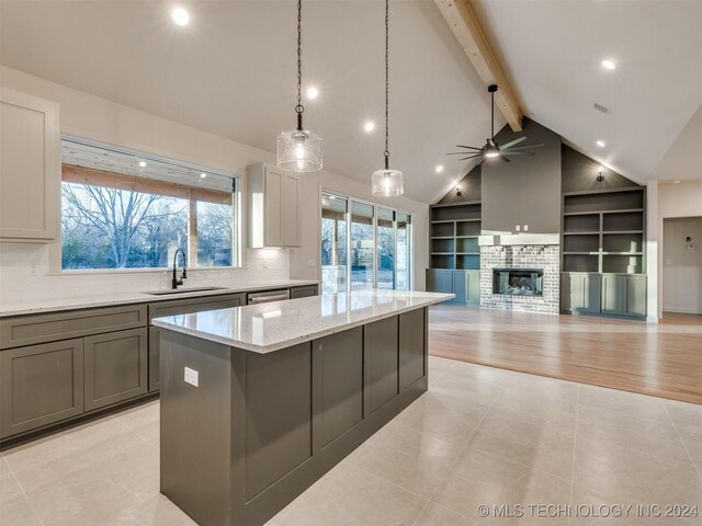 kitchen with light stone countertops, sink, beam ceiling, a kitchen island, and hanging light fixtures