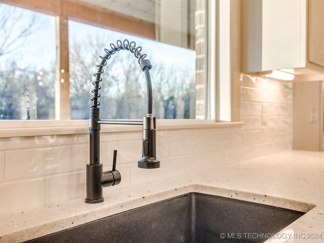 details featuring tasteful backsplash, white cabinetry, sink, and light stone countertops