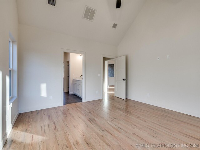 unfurnished bedroom featuring ensuite bathroom, high vaulted ceiling, and light hardwood / wood-style floors