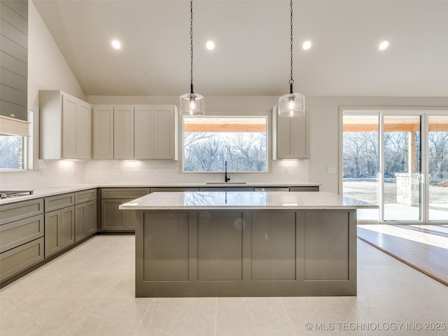 kitchen with light stone countertops, a kitchen island, a sink, vaulted ceiling, and backsplash