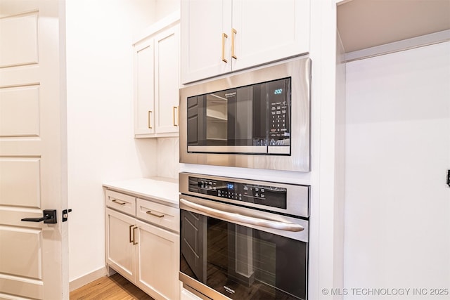 kitchen with white cabinets, oven, built in microwave, light countertops, and light wood-type flooring