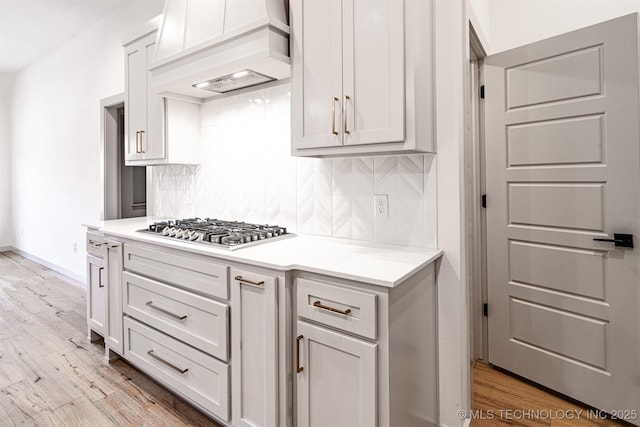 kitchen featuring custom exhaust hood, tasteful backsplash, light countertops, stainless steel gas stovetop, and light wood-style floors