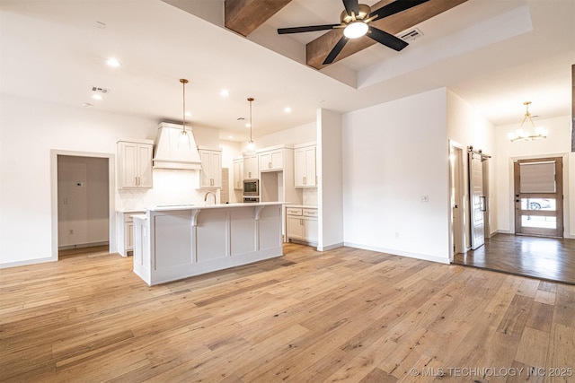 kitchen with a barn door, ceiling fan with notable chandelier, visible vents, light wood finished floors, and custom range hood