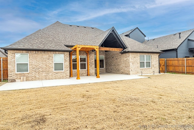 rear view of property with a shingled roof, fence private yard, brick siding, and a patio