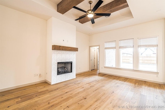 unfurnished living room featuring baseboards, wood-type flooring, ceiling fan, a tray ceiling, and a fireplace