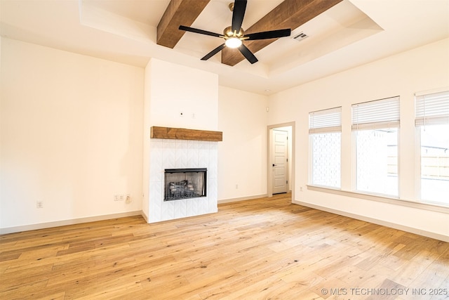 unfurnished living room featuring a premium fireplace, hardwood / wood-style floors, visible vents, baseboards, and a tray ceiling