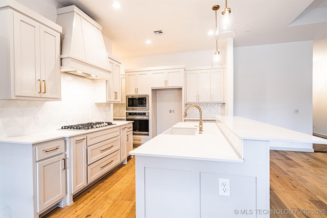 kitchen with stainless steel appliances, premium range hood, a sink, visible vents, and light wood-type flooring