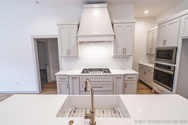 kitchen featuring a sink, custom range hood, stainless steel appliances, and backsplash