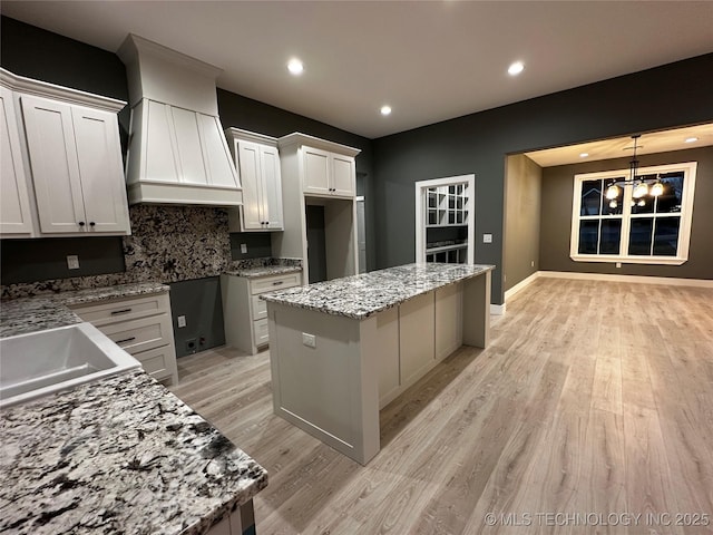 kitchen with backsplash, light stone counters, custom exhaust hood, white cabinets, and a center island