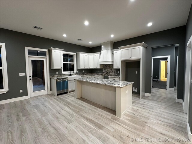 kitchen with white cabinets, stainless steel dishwasher, decorative backsplash, a kitchen island, and light stone counters