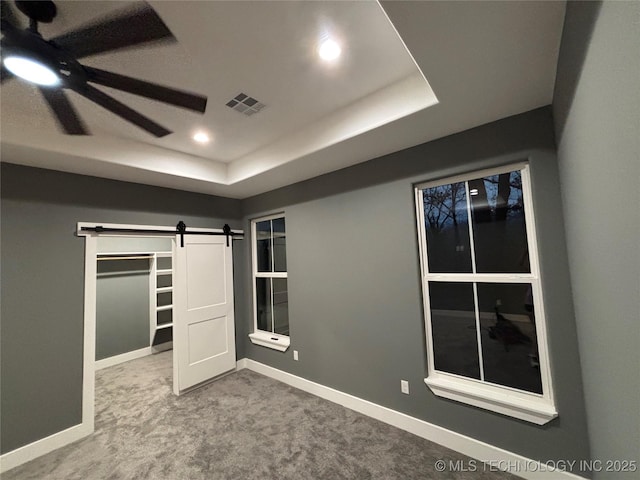 unfurnished bedroom with a barn door, a tray ceiling, ceiling fan, and carpet floors