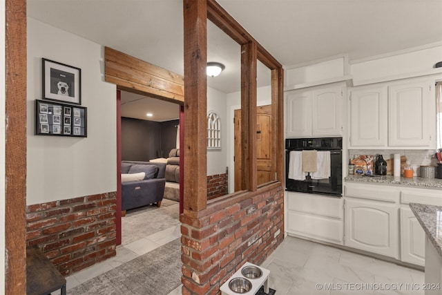 kitchen featuring white cabinets, decorative backsplash, black oven, and light stone counters