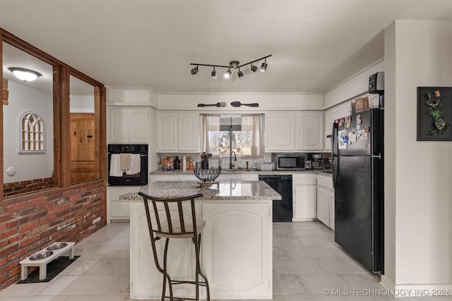 kitchen featuring black appliances, light stone countertops, a kitchen island, a kitchen bar, and white cabinetry