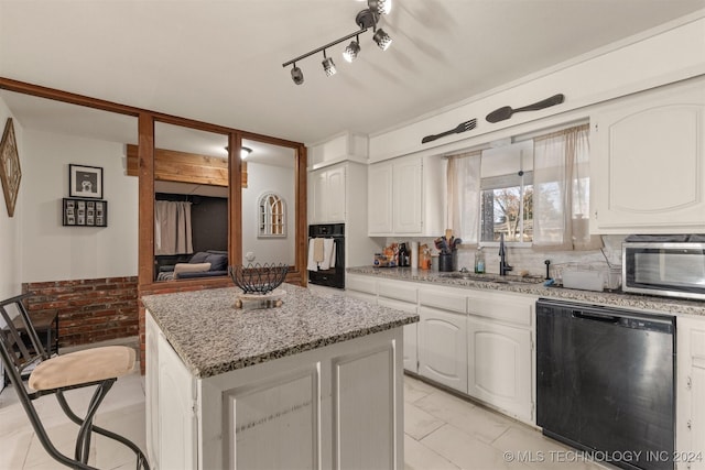 kitchen with light stone countertops, white cabinetry, sink, a center island, and black appliances