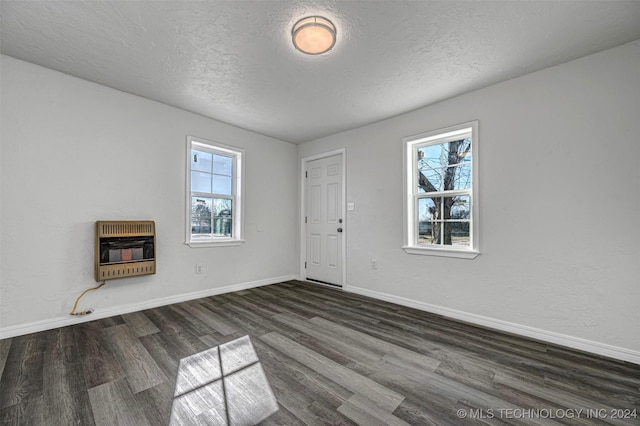 empty room with heating unit, dark hardwood / wood-style flooring, and a textured ceiling