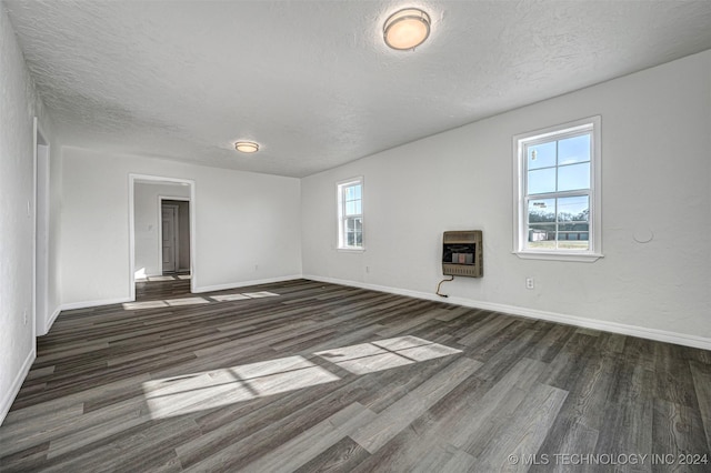 unfurnished room featuring heating unit, a wealth of natural light, dark hardwood / wood-style flooring, and a textured ceiling