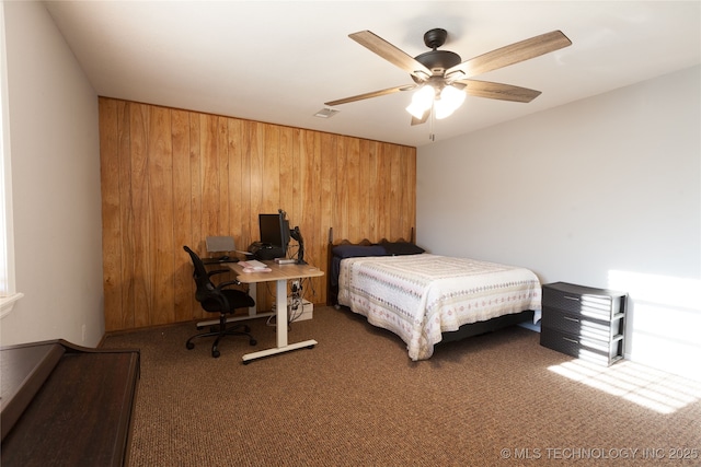 bedroom with wooden walls, ceiling fan, and dark colored carpet