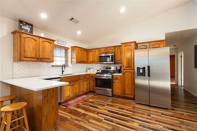 kitchen with kitchen peninsula, appliances with stainless steel finishes, decorative backsplash, sink, and lofted ceiling