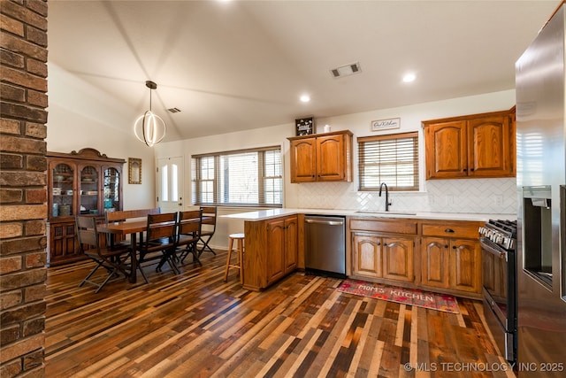 kitchen featuring kitchen peninsula, appliances with stainless steel finishes, tasteful backsplash, vaulted ceiling, and hanging light fixtures