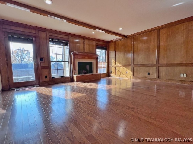 unfurnished living room featuring beamed ceiling, wood walls, and hardwood / wood-style flooring