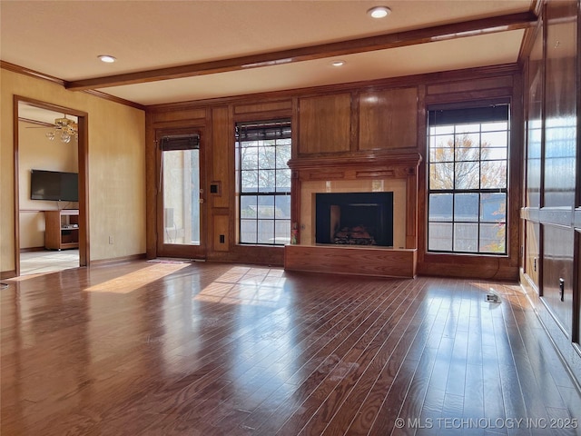 unfurnished living room featuring a wealth of natural light, wood walls, beamed ceiling, and wood-type flooring