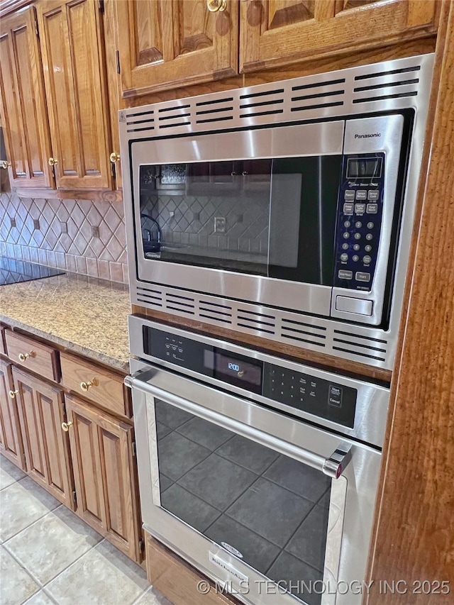 kitchen featuring decorative backsplash, light stone counters, light tile patterned floors, and appliances with stainless steel finishes