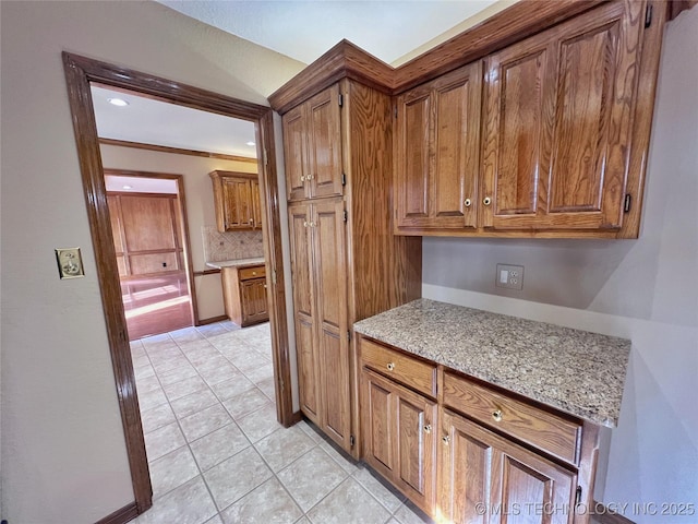 kitchen with tasteful backsplash, light stone countertops, light tile patterned floors, and ornamental molding