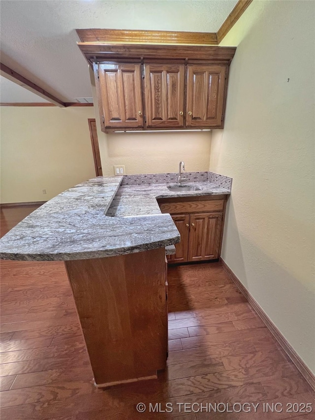 kitchen featuring light stone countertops, sink, dark hardwood / wood-style flooring, kitchen peninsula, and ornamental molding