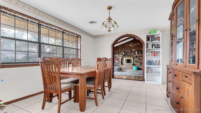 tiled dining space featuring a brick fireplace and a notable chandelier