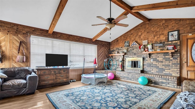 living room with wood walls, light hardwood / wood-style flooring, vaulted ceiling with beams, ceiling fan, and brick wall