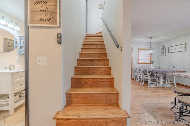 staircase with hardwood / wood-style flooring, a chandelier, sink, and a textured ceiling