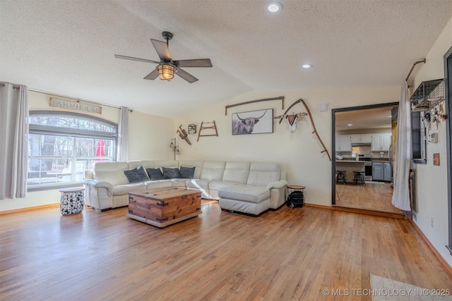 living room with a textured ceiling, light hardwood / wood-style floors, ceiling fan, and lofted ceiling