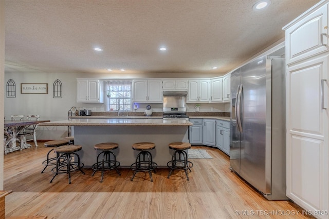 kitchen with white cabinetry, stainless steel fridge, and a kitchen bar