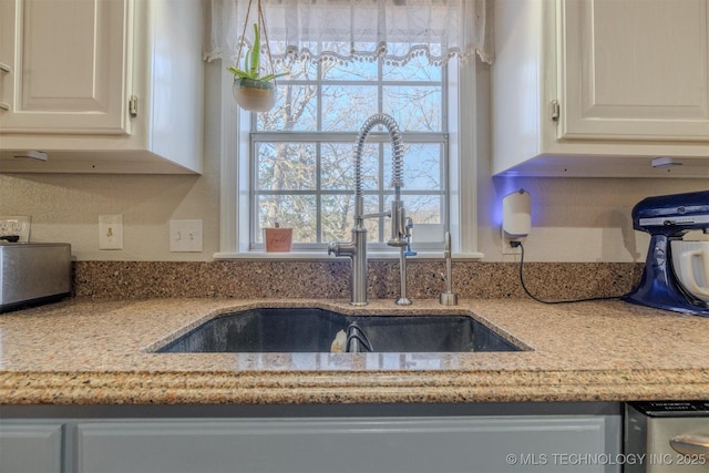 kitchen with white cabinets, light stone counters, and sink