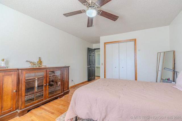 bedroom with ceiling fan, a closet, light hardwood / wood-style floors, and a textured ceiling