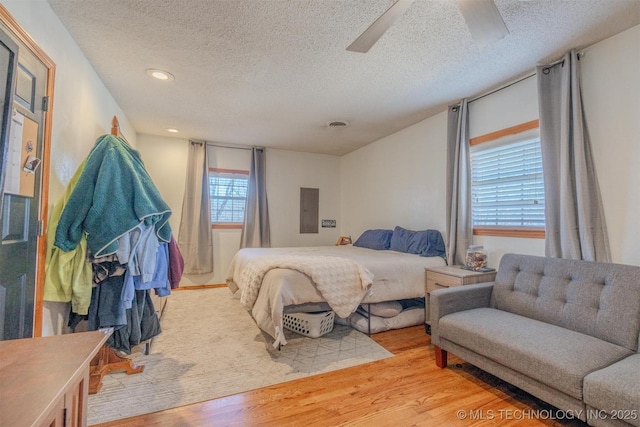 bedroom with a textured ceiling, light hardwood / wood-style floors, ceiling fan, and electric panel