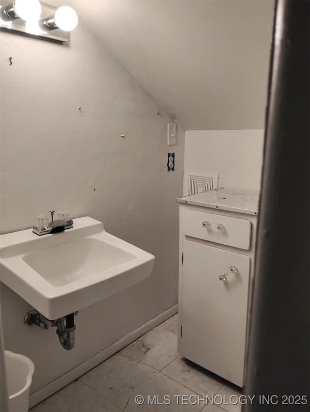 bathroom with tile patterned flooring, lofted ceiling, and sink