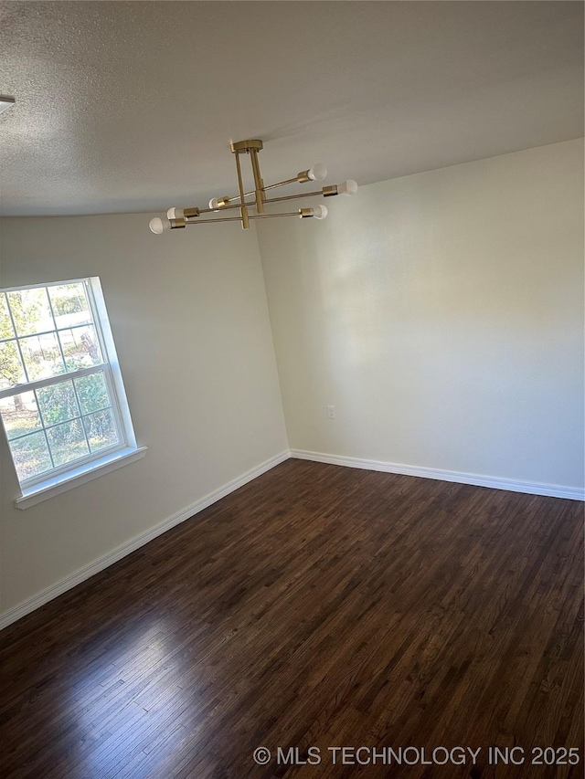 empty room with a textured ceiling, dark hardwood / wood-style flooring, and an inviting chandelier